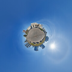 Fototapeta premium simple little tiny planet with buildings in blue sky with sun and beautiful clouds. Transformation of spherical panorama 360 degrees. Spherical abstract aerial view. Curvature of space.