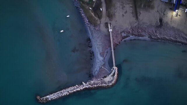 Top down aerial drone view of stone breakwater and pier structure in turquoise sea water at Roda beach