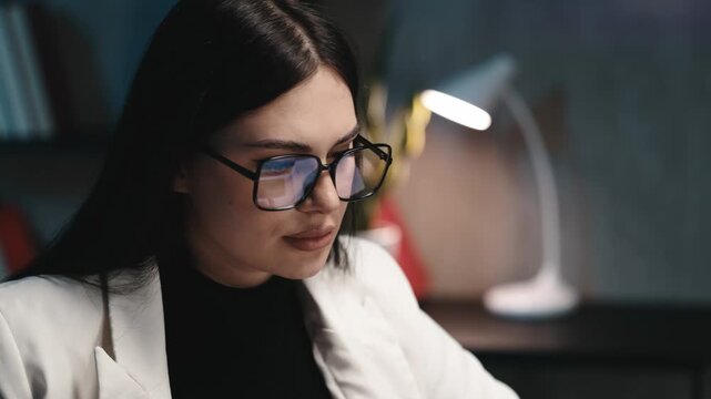 Businesswoman wearing glasses working late at computer in modern office close-up. Business productivity concept.
