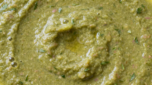 Macro background of fresh green herb sauce with spiral texture and olive oil drops