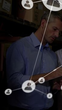 Vertical video: Warehouse mgr checking stock on clipboard, icon net starting across boxes  and  staf