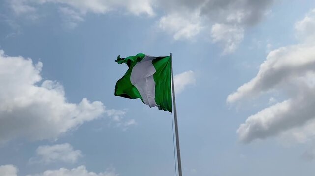 The Nigerian flag proudly waving in the wind, set against a serene blue sky with fluffy white clouds, symbolizing national pride and unity.