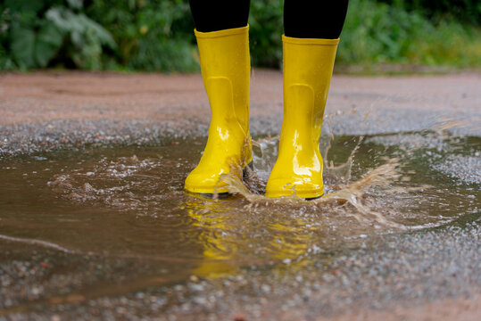 Bright yellow boots splashing in muddy puddle on path