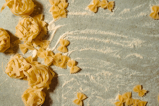 Various shapes of uncooked Italian pasta on a floured surface