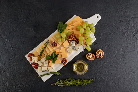 Cheese platter with grapes and nuts on a dark background