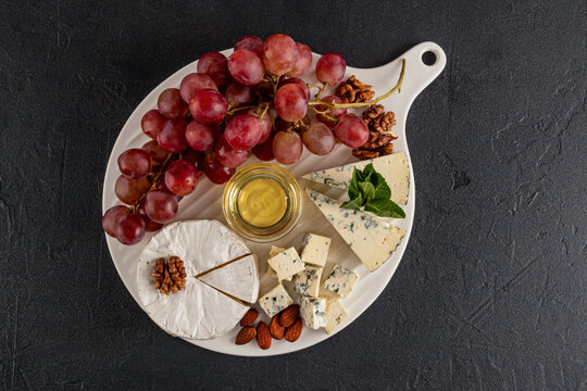 Cheese platter with grapes and honey on white board