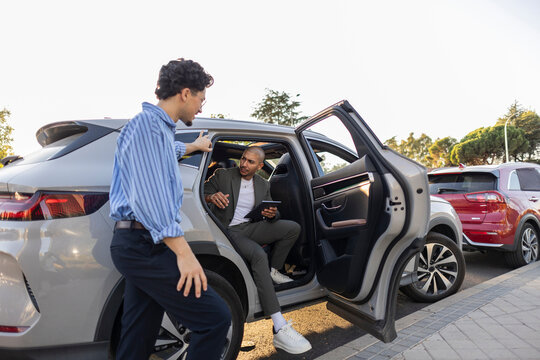 Businessmen interacting by car on city street