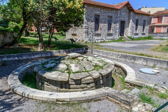 Circular archaic Funerary Monument of Menecrates from around 600 BC in front of historic stone buildings, Corfu, Greece