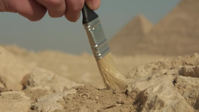 Archaeologist's hand with brush clearing sand particles from stone surface during excavations close-up