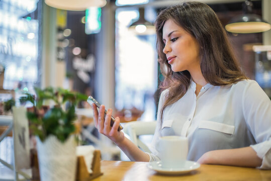 Woman in a cafe using smartphone and drinking coffee