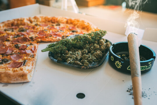 Cannabis joint and pizza on a table with ashtray