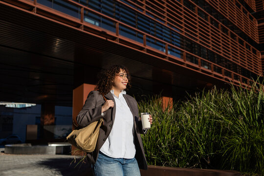 Confident businesswoman walking with coffee outdoors