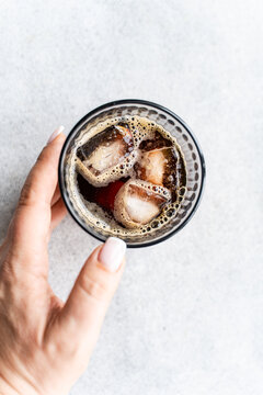 Hand holding glass of iced beverage from above