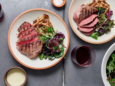 Sliced chuck steak with salad, mushrooms and red wine glass.