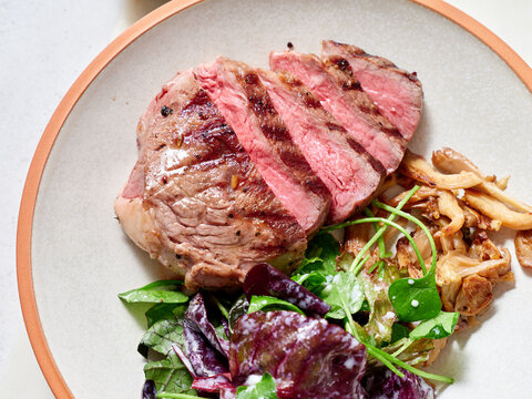 Sliced chuck steak with salad, mushrooms.