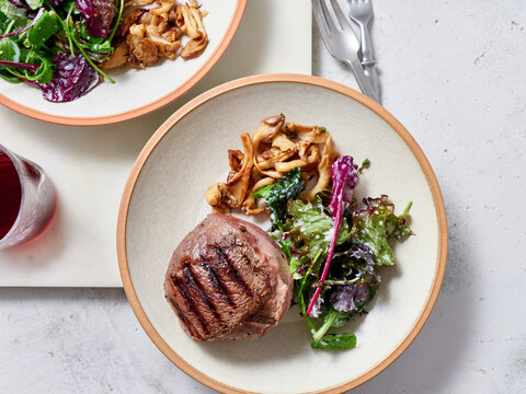 Sliced chuck steak with salad, mushrooms and wine.