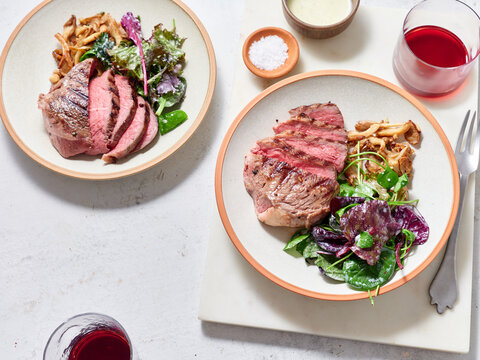 Sliced chuck steak with salad, mushrooms and red wine glass.