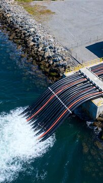 Vertical video: Releasing hose pack sending big flow at rocky shore with pumps starting, copy space