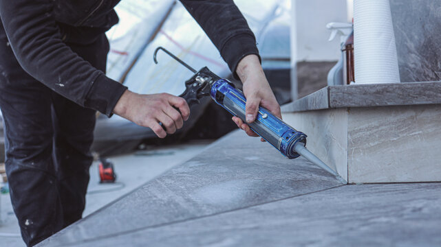 Construction worker applying sealant with a caulk gun to outdoor stone steps