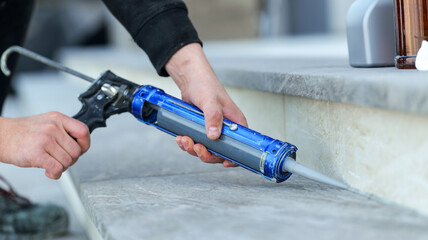 Fototapeta premium Hand applying sealant with a caulk gun to outdoor stone steps for weatherproofing