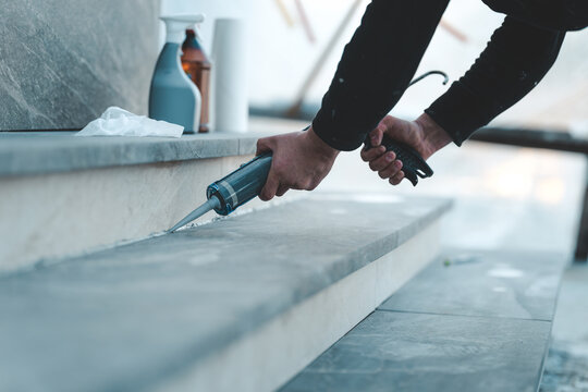 Construction worker applying sealant to outdoor stone steps with a caulking gun