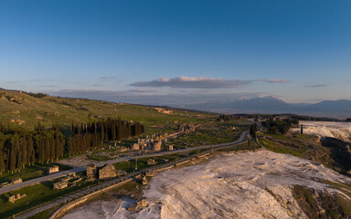 Aerial drone view of Hierapolis Antik Kenti and the famous Pamukkale travertines in Denizli, Turkey, showing ancient ruins, Roman theater, columns, and scenic landscape from above.