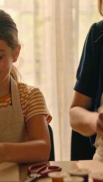 Vertical video: Noticing loose strap, parent adjusting apron and guiding child at table with thread
