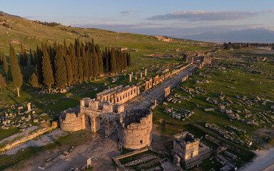 Aerial drone view of Hierapolis Antik Kenti and the famous Pamukkale travertines in Denizli, Turkey, showing ancient ruins, Roman theater, columns, and scenic landscape from above.