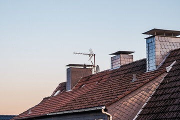Rooftops with chimneys and antennas against a clear sky at dusk