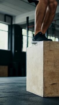 Vertical video: Jumping male athlete starting beside plyo box, landing on rubber floor for training