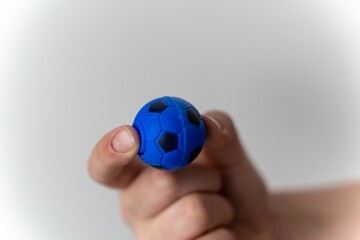 Fototapeta premium Child's hand holds a small blue soccer ball toy in a simple indoor setting