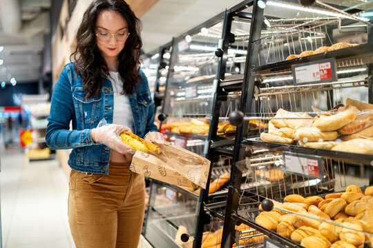 Woman buying fresh bread at a grocery store bakery section choosing food
