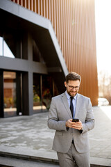 Businessman checks phone outside modern office building during daytime hours