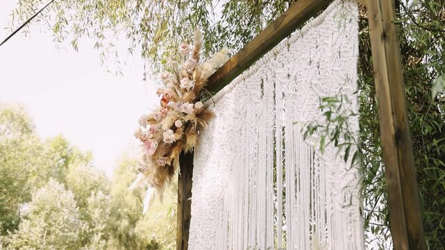 Wooden arch canopy floral crown macrame fringe and willow branches. Pale roses and dried grasses woven into