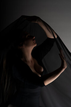 Mysterious curvy woman holding flowing black veil in dark studio, dramatic low key portrait