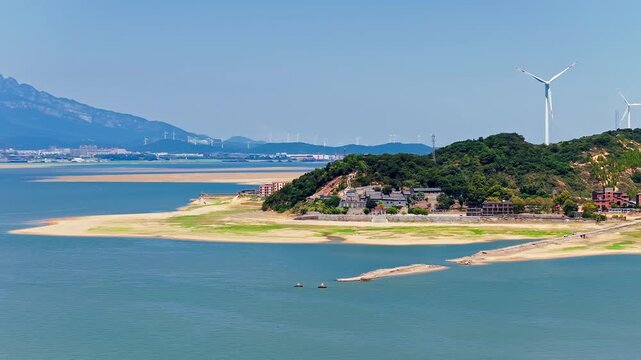 Scenic landscape of wind turbines on green hills by the sandy banks of Poyang Lake, highlighting renewable energy and natural beauty in Jiujiang, China.