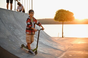A boy on a scooter in skate park at sunset. The concept of a healthy lifestyle and sports leisure © Serhii