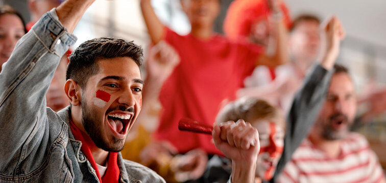 Excited football fans supproting Austrian national team in live soccer match at stadium.