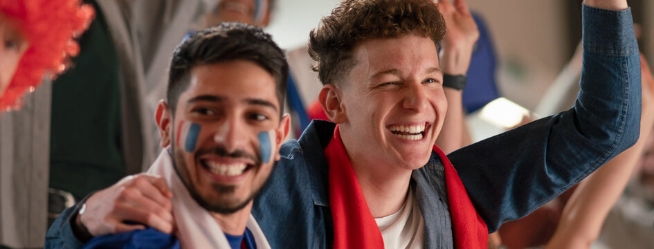 Excited football fans supproting French national team in live soccer match at stadium.