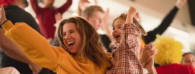 Excited football fans, mother with little daughter, supporting German national team in live soccer match at stadium. © Halfpoint