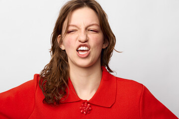 Young woman in red sweater makes funny face with eyes closed and mouth twisted. Studio portrait on...