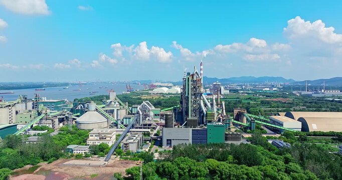 High angle view of modern industrial factory complex located by the river bank with cargo ships and lush green environment.