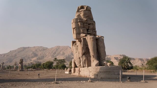 Massive stone statue of Colossus of Memnon in Egypt, depicting pharaoh seated on throne
