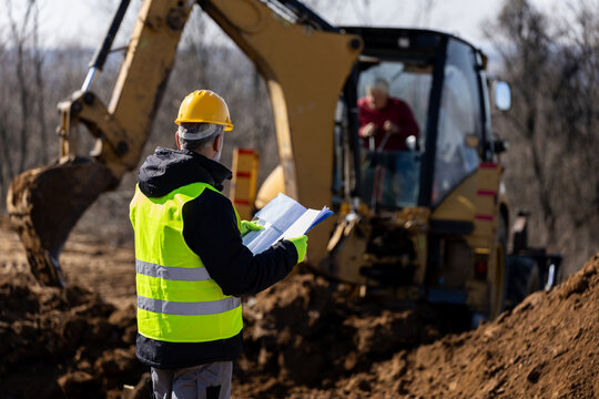 Site supervisor coordinating excavator operator during trench excavation