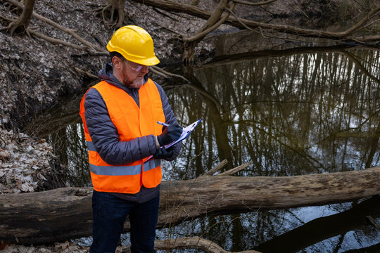 Environmental engineer in hardhat and safety gear conducting river monitoring in a spring forest. Specialist is recording data on meltwater levels and aquatic ecology to assess flood prevention.