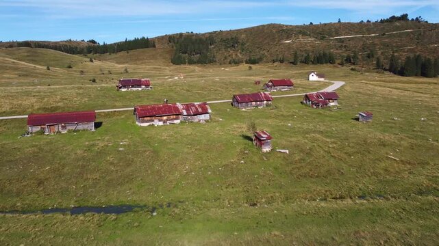 Aerial drone footage flying over the Marcesina plateau in Italy, showcasing the iconic "Casoni" mountain huts. The video captures the peaceful, isolated nature of these ancient rustic cabins