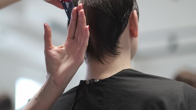 Close up of a professional hairstylist using scissors and a blue comb to cut dark hair in a salon