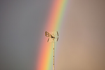 Fototapeta premium Vibrant Vertical Rainbow Over European Rooftops with Antenna at Golden Hour