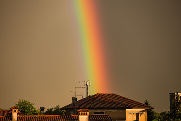 Fototapeta premium Rainbow in sky clouds over Vibrant Vertical Rainbow Over European Rooftops at Golden Hour village houses