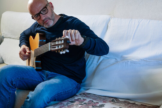 Man tuning acoustic guitar on couch at home